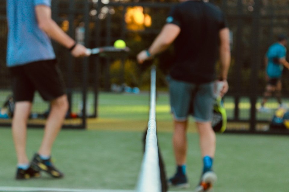 Padel players mid-rally on an outdoor court at golden hour