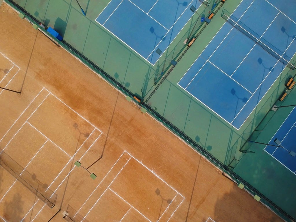 Aerial view of blue hard courts and red clay tennis courts at a multi-court academy